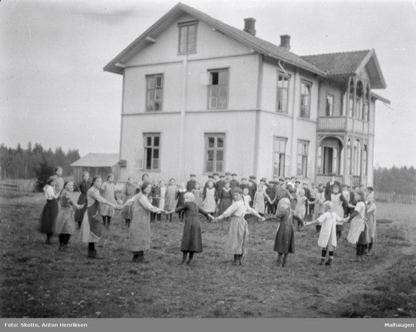 Bildet viser barn i lek utenfor den gamle Jønsrud skole, ca 1920, fra Digitalt museum, Anno museum.